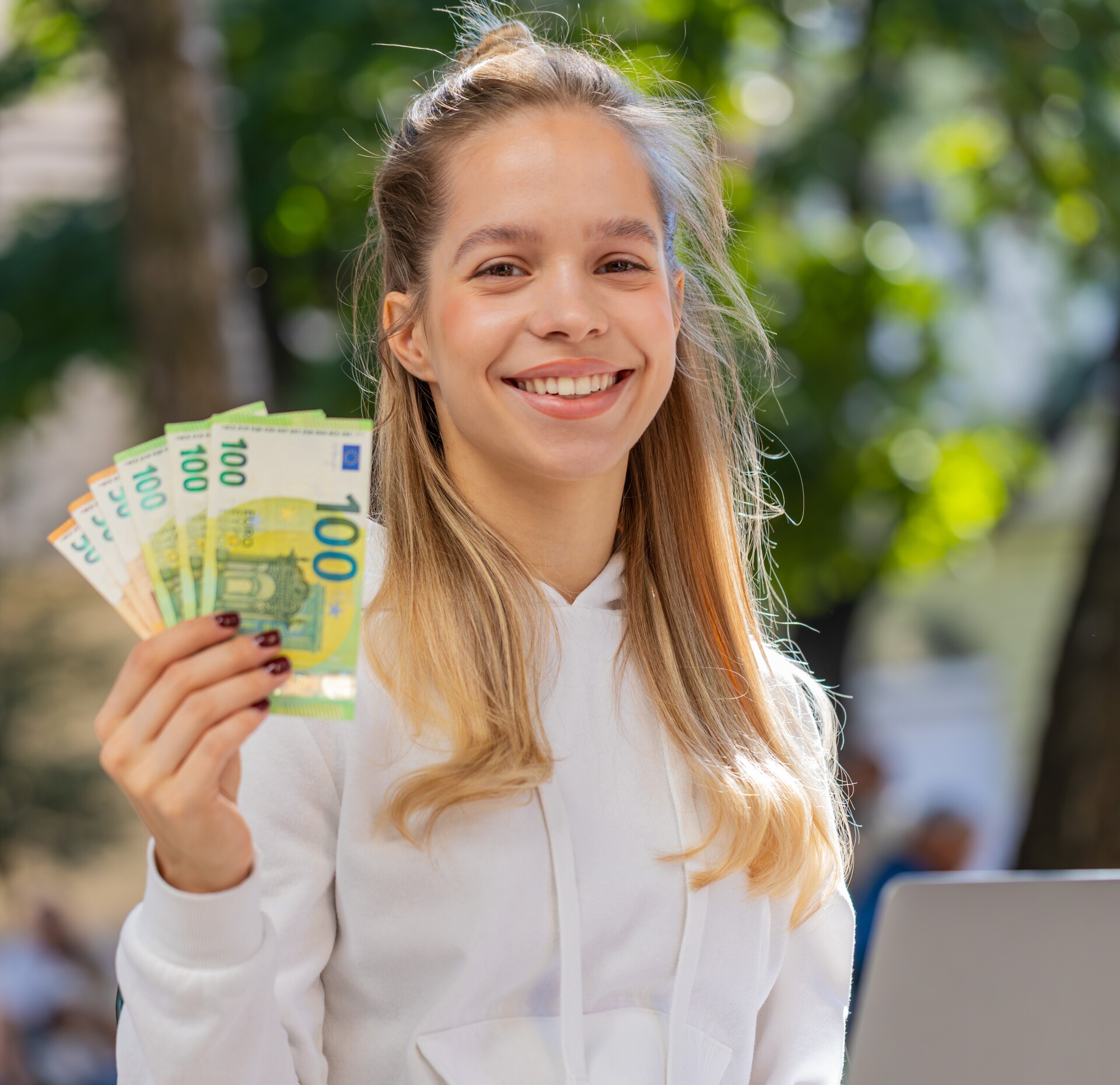 Happy rich woman using laptop winner victory holding cash money euro banknotes sitting chair