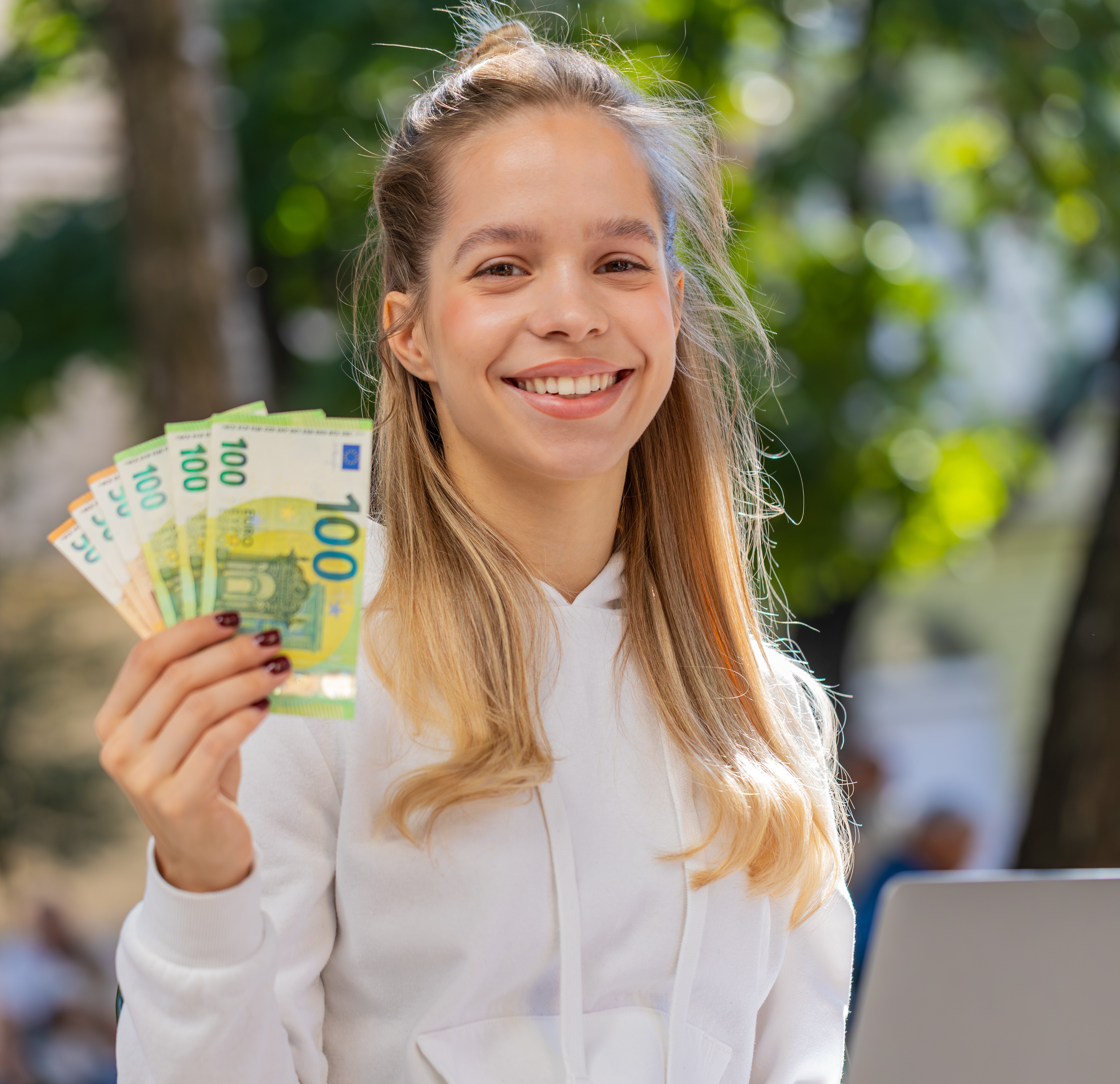 Happy rich woman using laptop winner victory holding cash money euro banknotes sitting chair